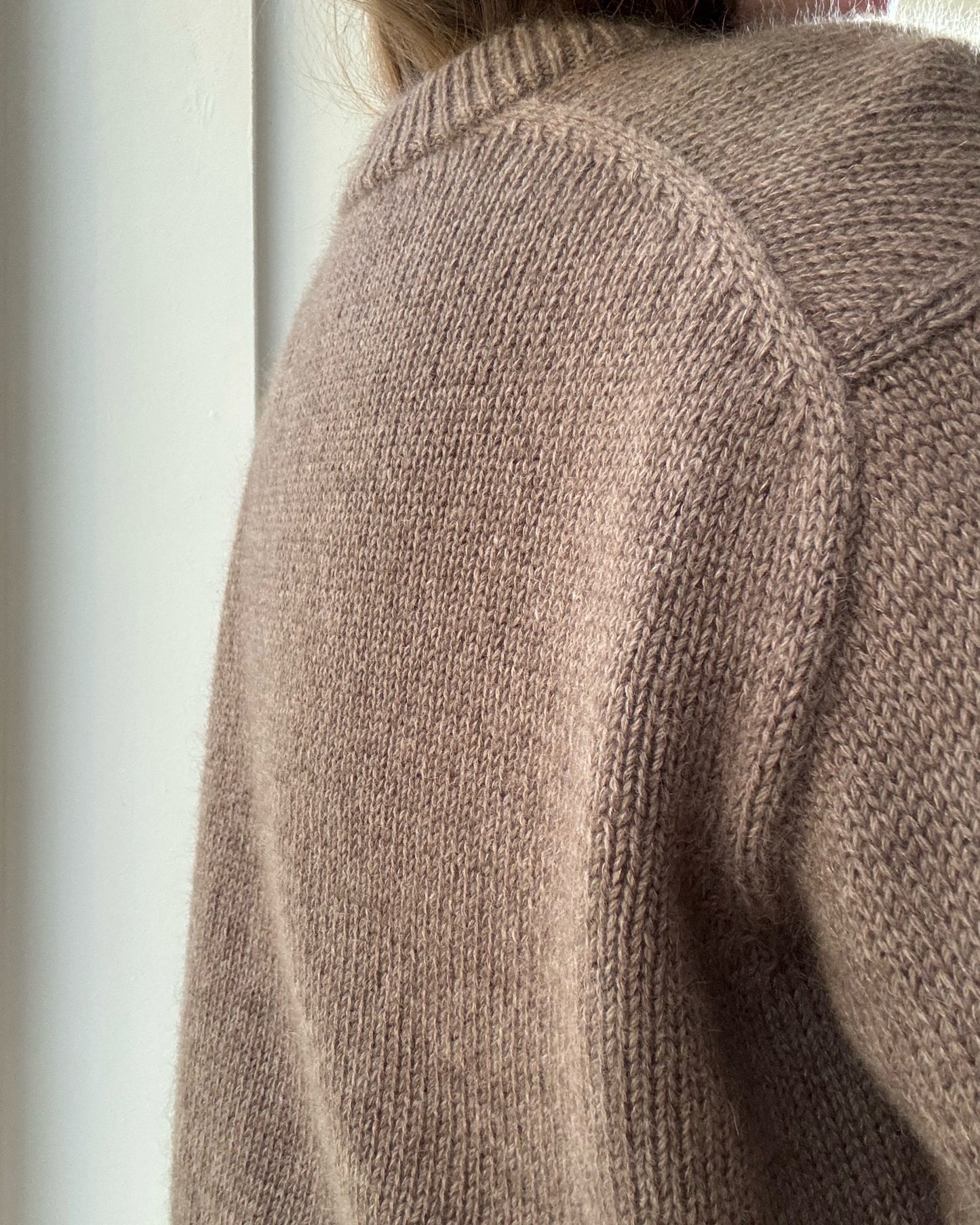Cropped head frame focuses on sleeve and cuff showing double knitting rib and soft fabric in wool and mohair.
