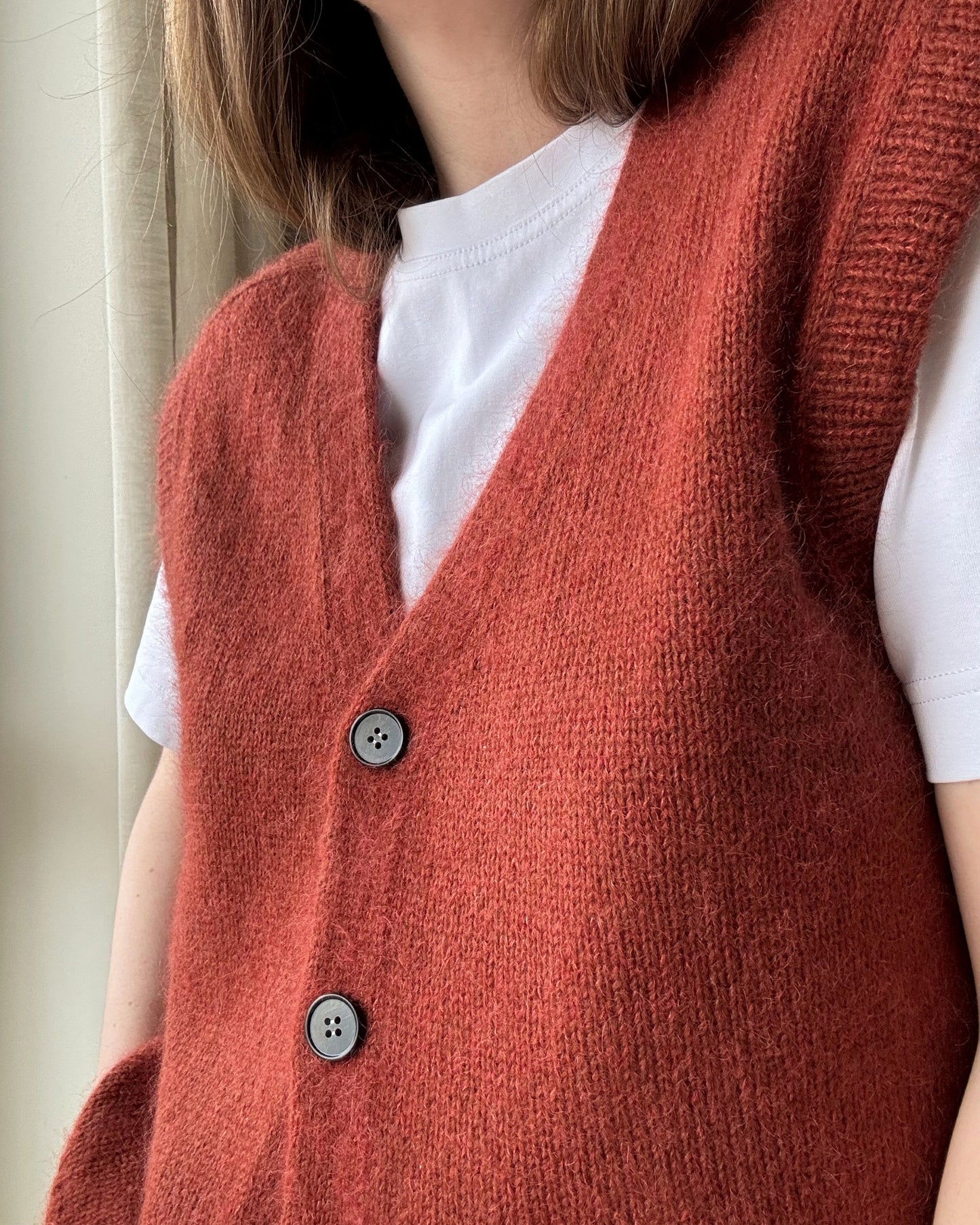 Fortgeschrittenes Muster für einen ärmellosen Cardigan, der klassisches Design mit weichen, glatt rechten Strickdetails kombiniert.