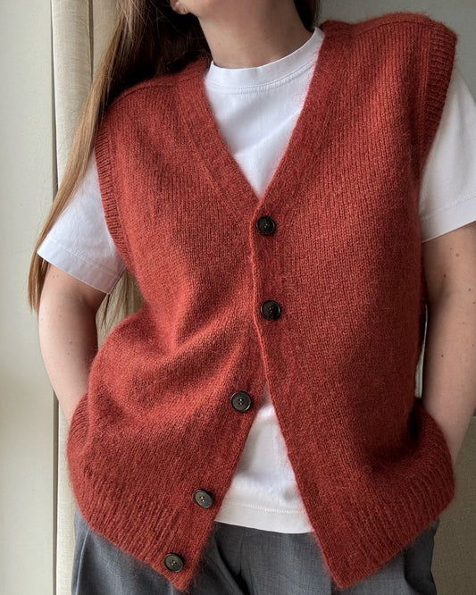 Avancerat mönster för en ärmlös cardigan som kombinerar klassisk design med mjuka slätstickade detaljer.