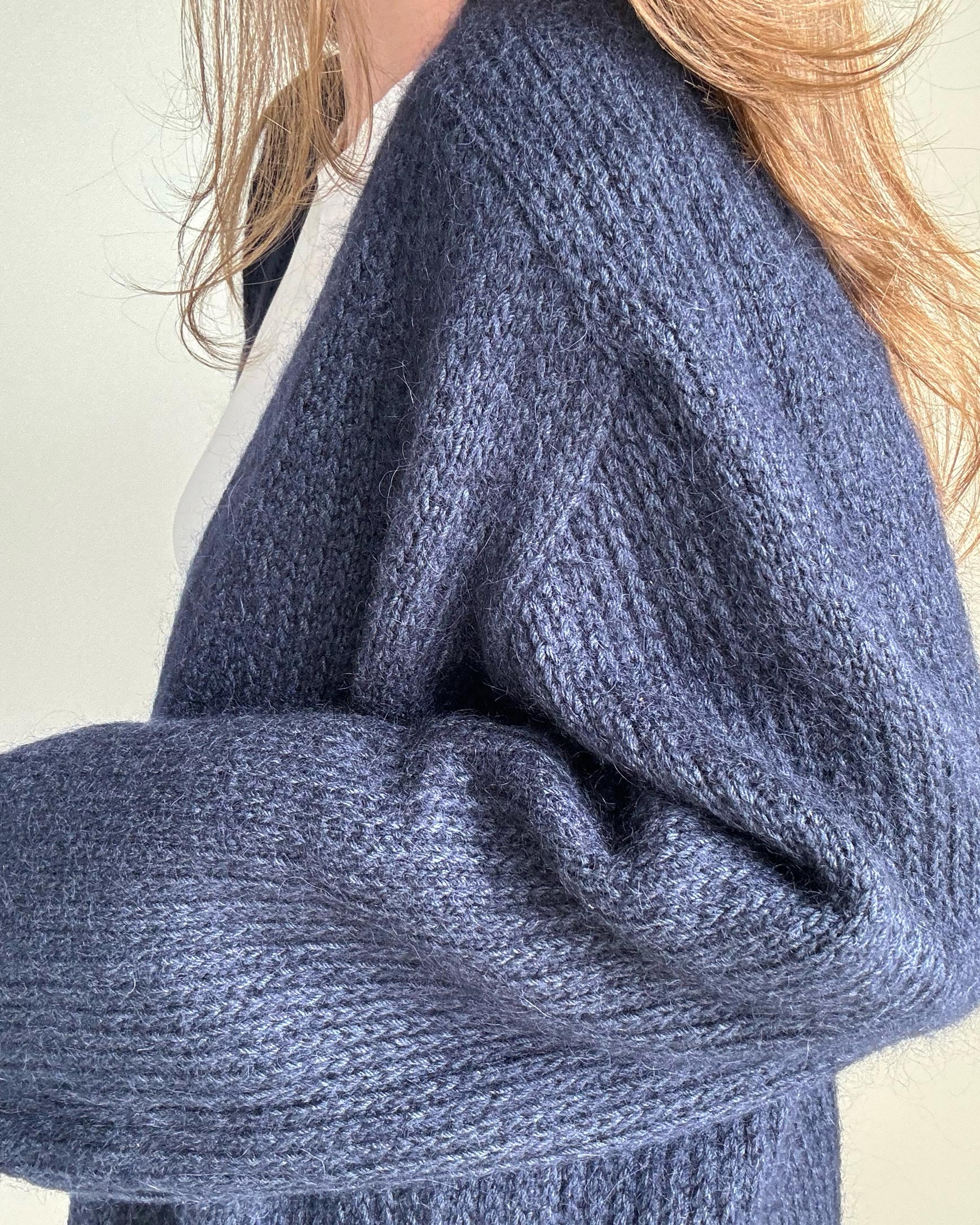 Anleitung für das Stricken eines zeitgenössischen, marineblauen Cardigans mit offener Front.