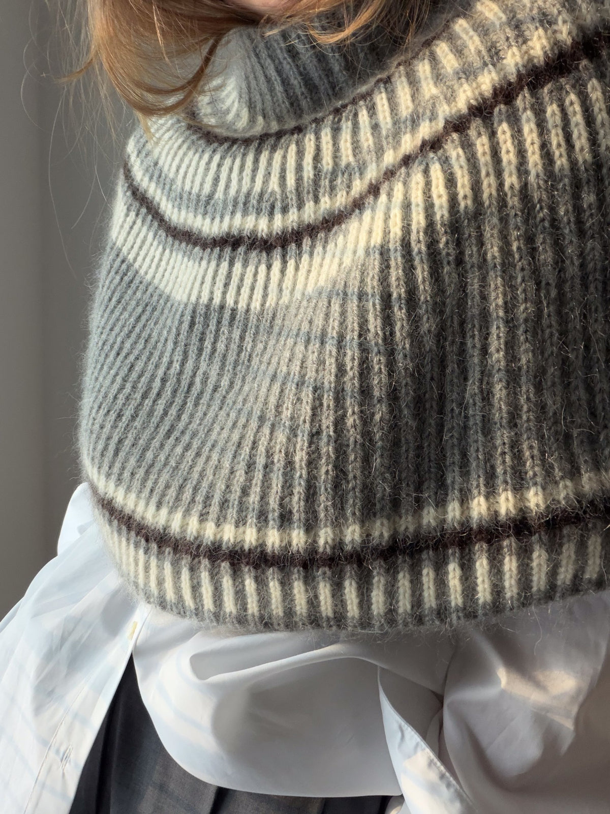A model stands in a relaxed pose wearing the capelet over layered clothing.