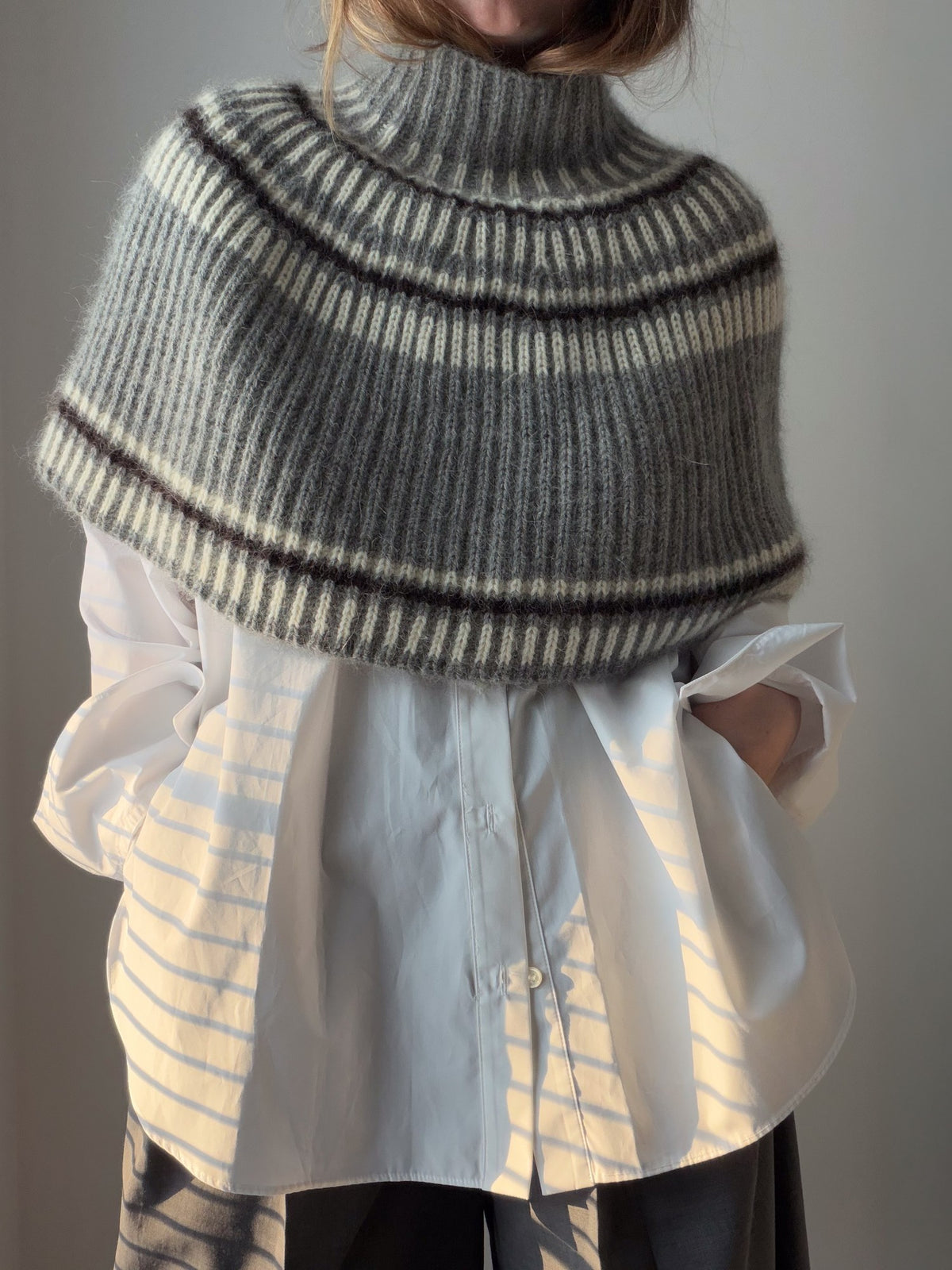 A model wears a textured capelet with a high turtleneck in a relaxed front view.