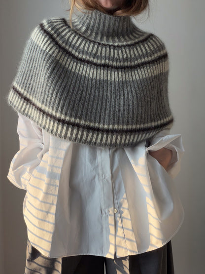 A model wears a textured capelet with a high turtleneck in a relaxed front view.