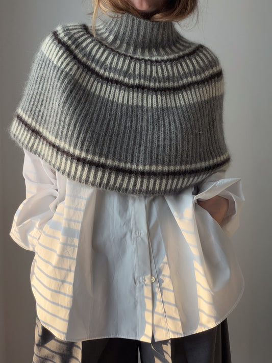 A model wears a textured capelet with a high turtleneck in a relaxed front view.