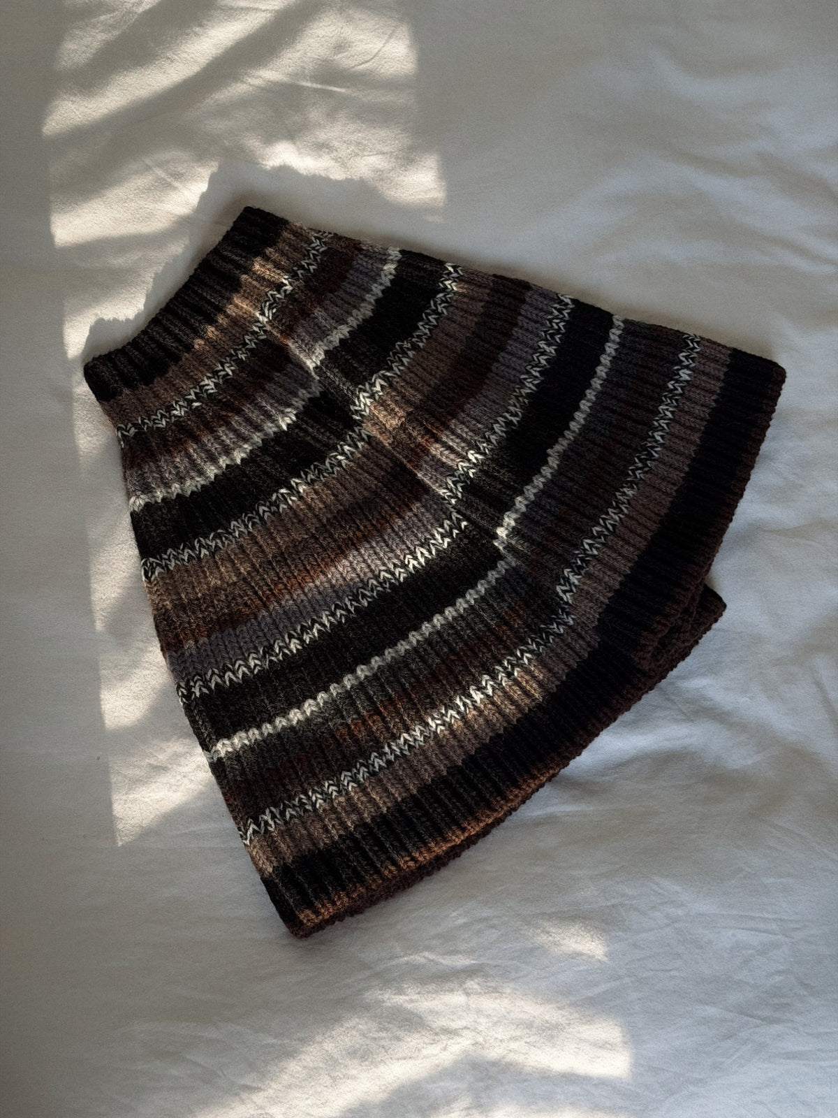 Front view of the striped capelet showing the high neck, compact length, and textured surface.