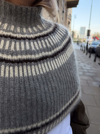Front detail showing the capelet draping around the upper body with a gently flared shape.