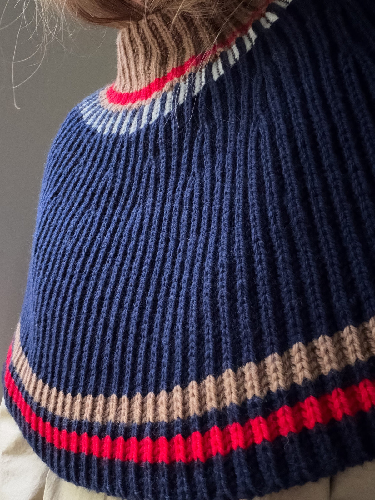 Three quarter view of the capelet showing the high neck, horizontal stripes, and rounded silhouette.