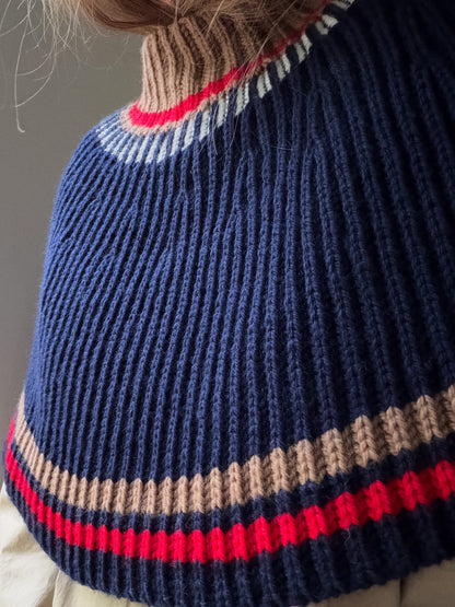 Three quarter view of the capelet showing the high neck, horizontal stripes, and rounded silhouette.